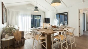 Un comedor con una mesa de madera, sillas blancas e iluminación colgante.