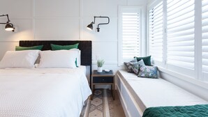 Un dormitorio con cama, mesitas de noche, lámpara de pared y ventana con persianas.