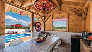 A wooden cabin with a pool, a table with fruit, and a large wheel. - Stunning home in Gospic with sauna (Gospic)