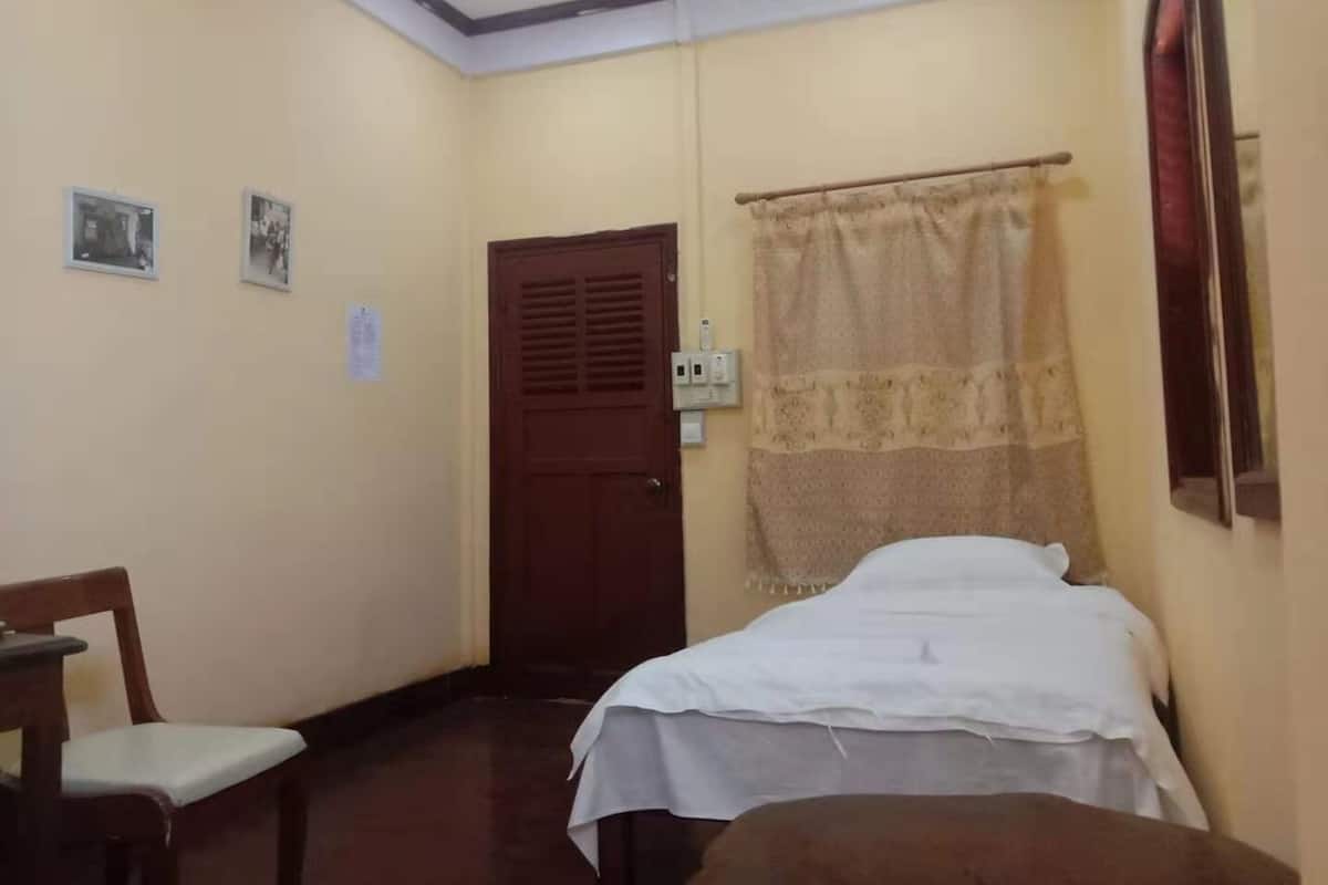 A room with a bed, a chair, a wooden door, and a ceiling fan.