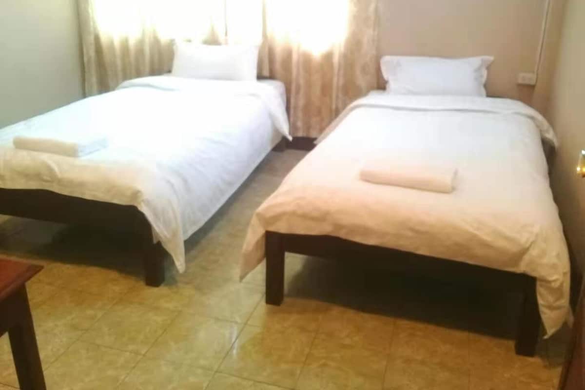 A room with two single beds, each with a white duvet and a folded towel.