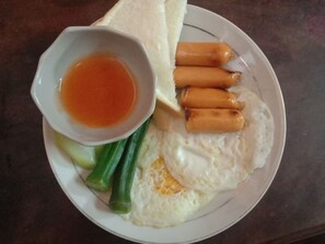 A plate with a fried egg, sausage, green vegetables, and a small bowl of sauce. - Green Land Hotel (Vientiane)