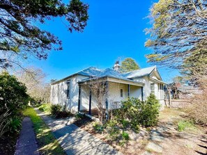 A single-story house with a front porch, a visible chimney, and a pathway leading to the entrance.