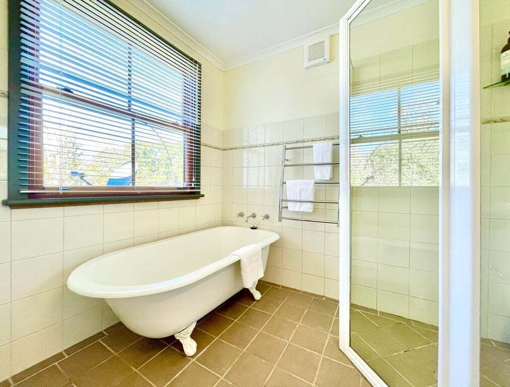 Un baño con bañera independiente, cabina de ducha con paredes de cristal y una ventana con persianas.