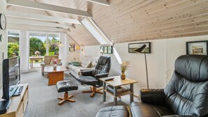 En hyggelig loftstue med højt til loftet, træbjælker, en sofa, en læderlænestol, et sofabord og et fjernsyn.