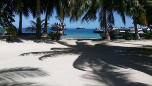 A beach with palm trees, a sandy path, and boats in the water. - Pension Chez Glorine (Rangiroa)
