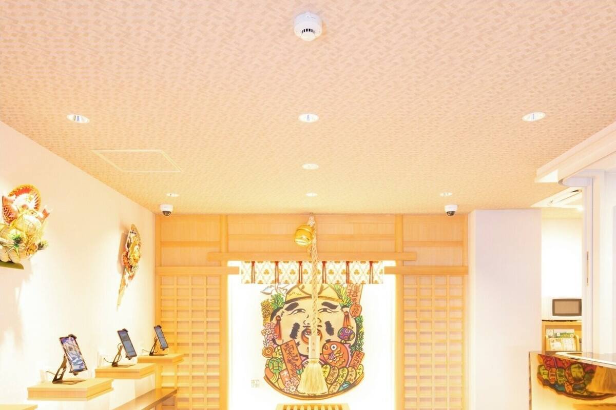 A reception area with a traditional Japanese-style mural, wooden shelving with electronic devices, and a tiled floor.