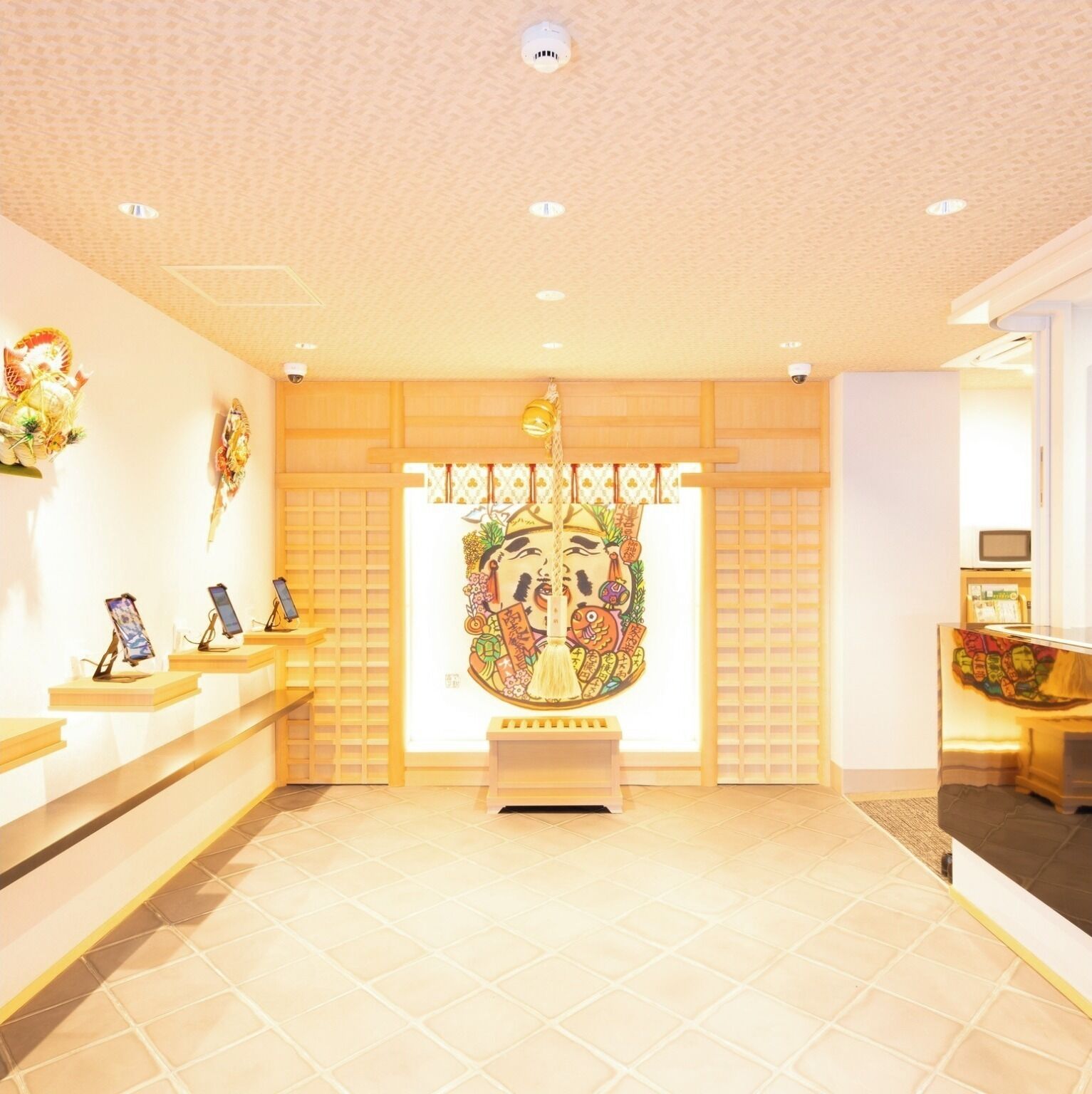 A reception area with a traditional Japanese-style mural, wooden shelving with electronic devices, and a tiled floor.