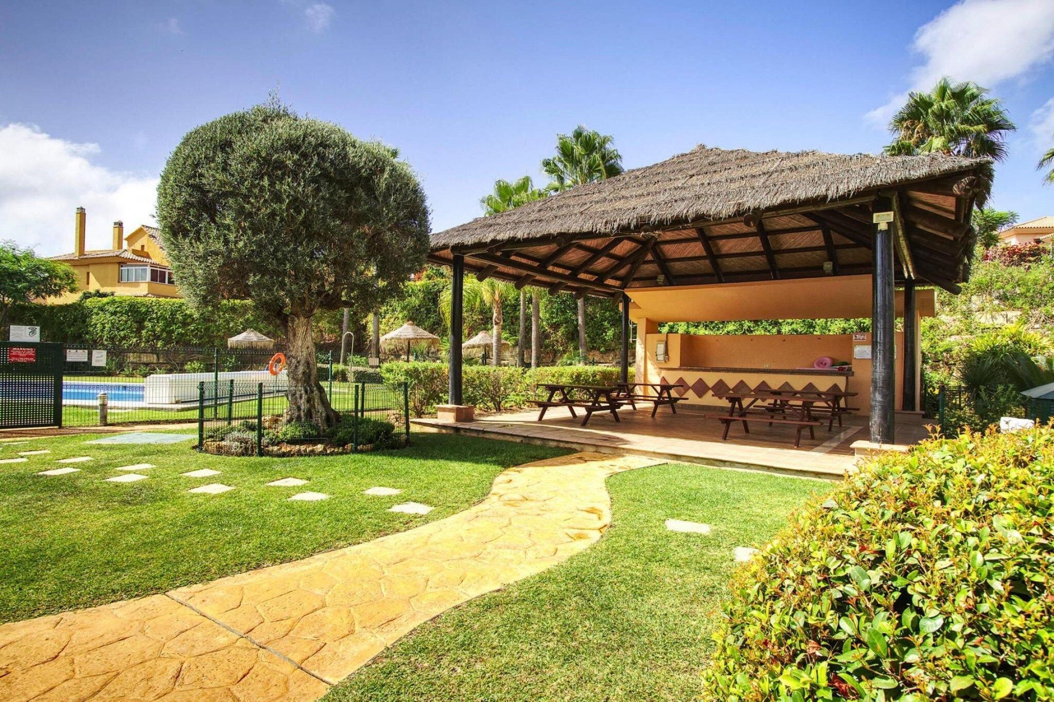 A covered outdoor seating area with picnic tables, a pathway, and a well-maintained lawn.