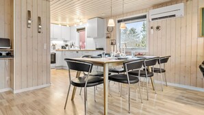 A modern kitchen with wooden paneling, a dining area with black chairs, and a large window providing natural light.