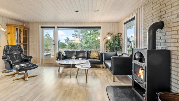 A cozy living room with a fireplace, leather furniture, and large windows offering a view of the outdoors.