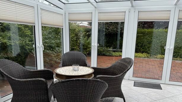 A conservatory with wicker furniture and a glass table.