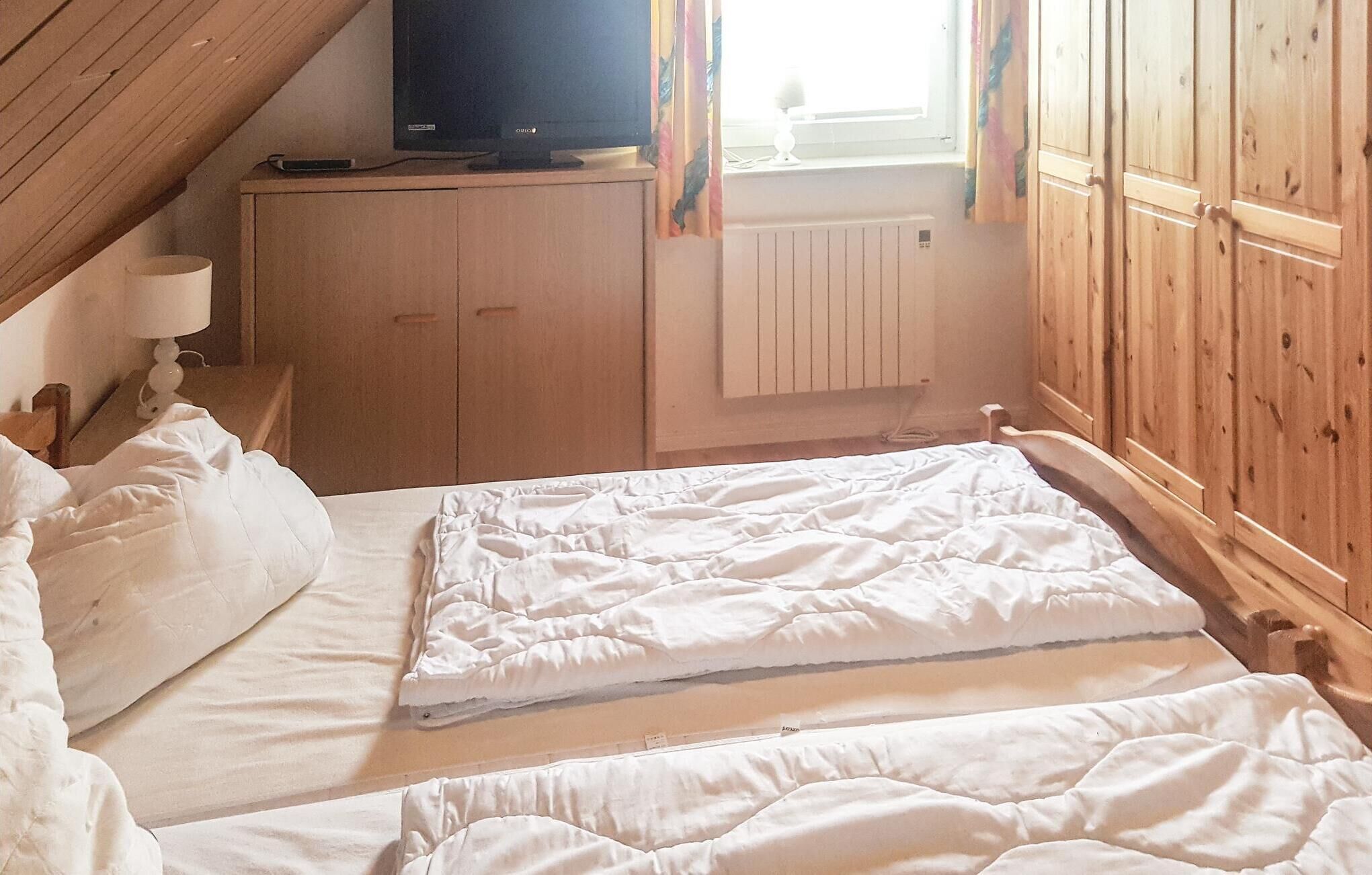 Ein Schlafzimmer mit zwei Betten, einem Holzschrank, einem Fernseher auf einem Schrank und einem Fenster mit Vorhängen.