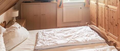 Ein Schlafzimmer mit zwei Betten, einem Holzschrank, einem Fernseher auf einem Schrank und einem Fenster mit Vorhängen.