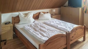 En säng i trä med vita sängkläder i ett rum med träväggar och ett sluttande tak.