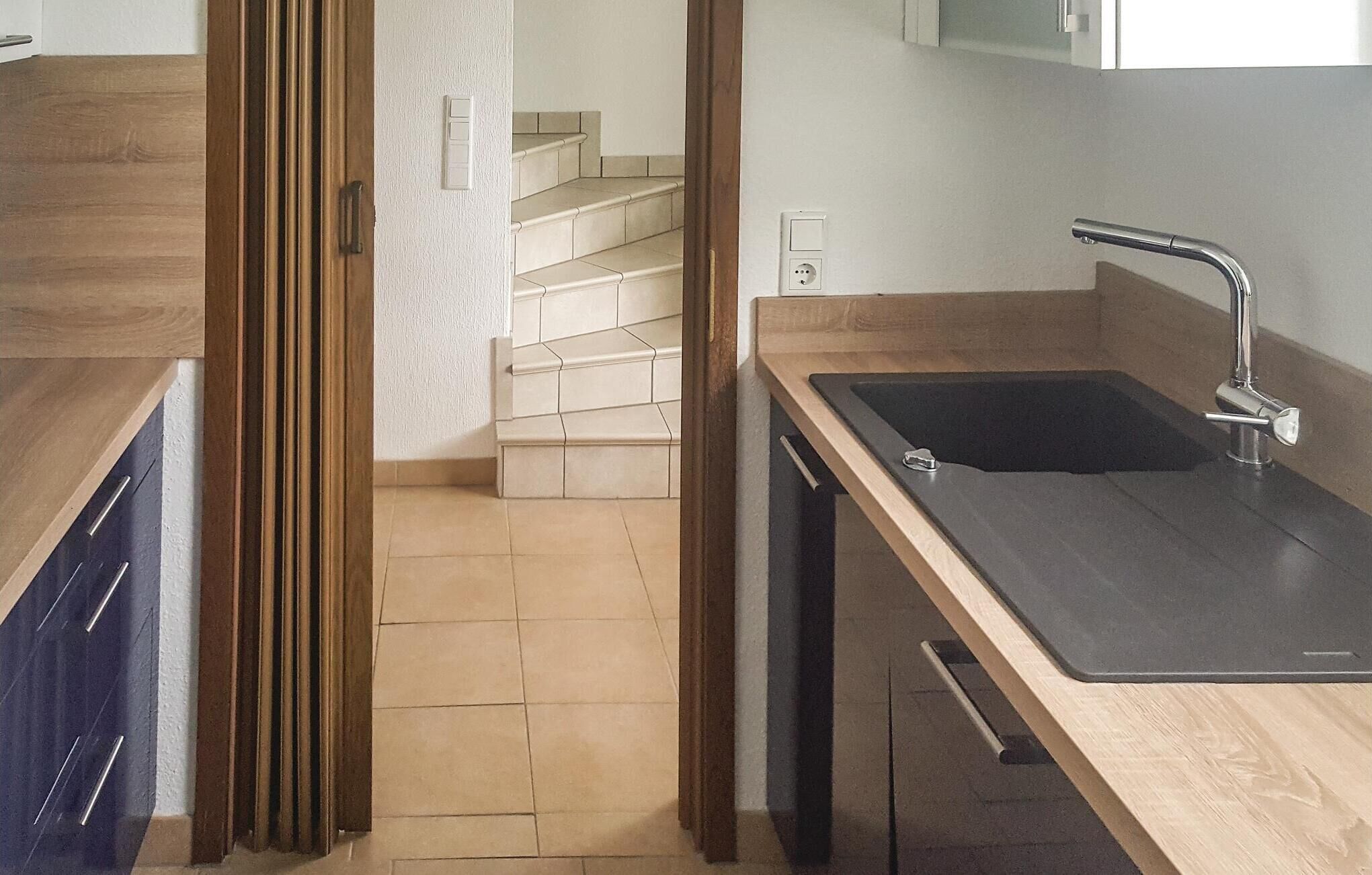 Une cuisine moderne dotée d’un plan de travail en bois, d’un évier noir et d’un escalier menant à un niveau supérieur.