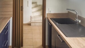 Ett modernt kök med en bänkskiva i trä, en svart diskho och en trappa som leder upp till ett övre plan.
