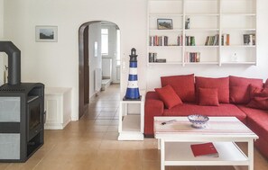 A living room with a red sofa, a white coffee table, a bookshelf, and a black stove. - 2 bedroom cozy home in Nordstrand (Nordstrand)