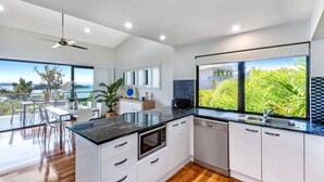 A modern kitchen with a large island, white cabinetry, and a view of greenery through the windows. - Pinnacle 4, Seaview Apartment on Hamilton Island (Hamilton Island)