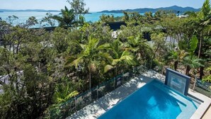 A pool surrounded by lush greenery and a view of the ocean. - Pinnacle 4, Seaview Apartment on Hamilton Island (Hamilton Island)