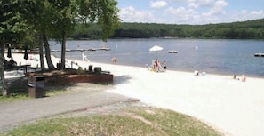 Un parque junto al lago con mesas de picnic, una rampa para embarcaciones y gente relajándose en la arena.