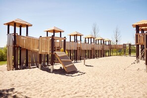 Una estructura de juego de madera con varios niveles y toboganes sobre una playa arenosa.