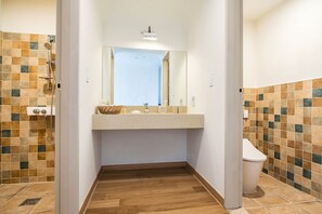 A narrow bathroom with a tiled shower wall, a wooden floor, a sink with a mirror, and a toilet. - Club ES Jeju Resort (Seogwipo)