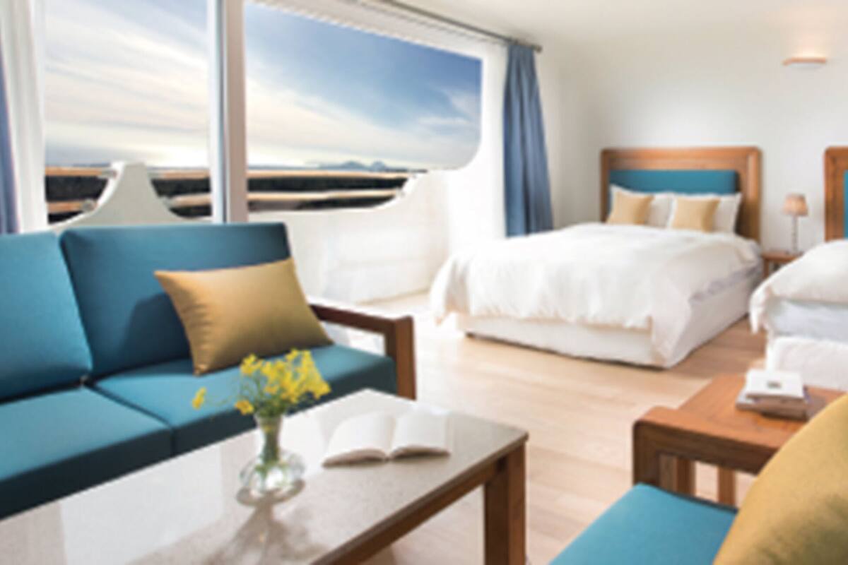 A hotel room with two beds, a sofa, a coffee table, and a view of the sea.