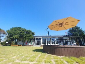 A building with a glass facade, outdoor seating area, and a large yellow umbrella. - Jeju Eoeumbungyo 1963 Guesthouse (Jeju City)