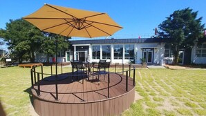 A circular wooden deck with a table and chairs, an umbrella, and a building in the background. - Jeju Eoeumbungyo 1963 Guesthouse (Jeju City)
