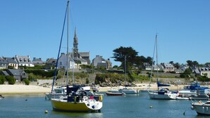 A coastal marina with various boats docked, a sandy beach, and houses in the background.