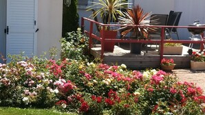 A garden with a variety of flowers, a wooden deck with chairs, and a barbecue grill.