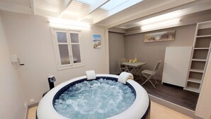 A hot tub in a room with a skylight, a window, a painting, and a small table with drinks.