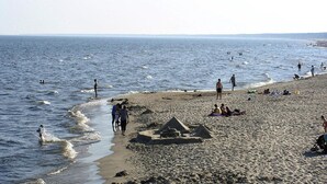 A beach with people walking along the shore, some in the water, and sand structures on the beach.