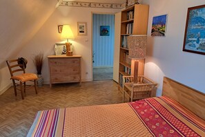Ein gemütliches Schlafzimmer mit Bett, einem Holzschrank, einem Stuhl, einem Bücherregal und einer Lampe.