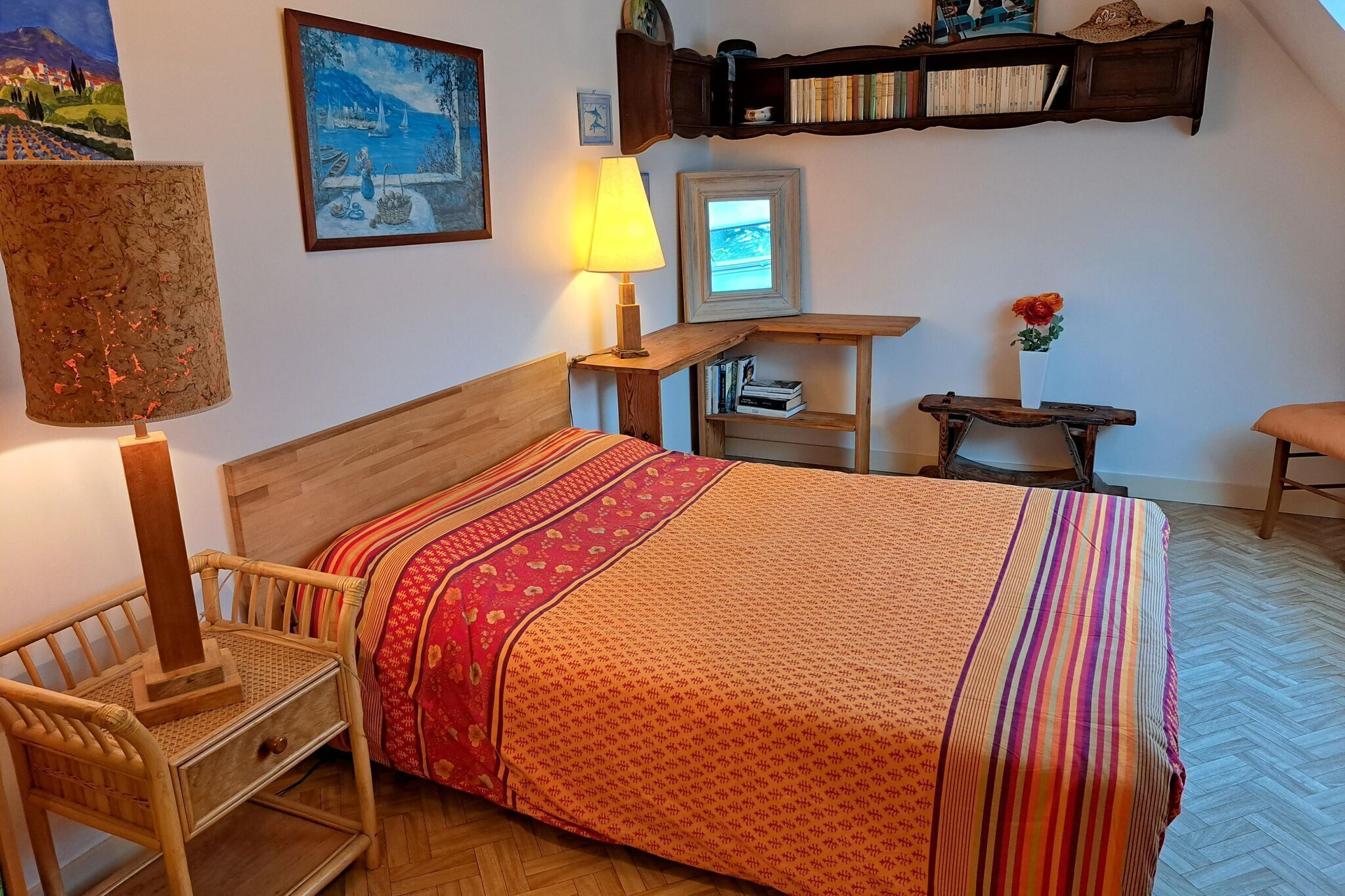Une chambre à coucher avec un lit en bois, une table de chevet, une chaise, une lampe et une étagère avec des livres et un vase.