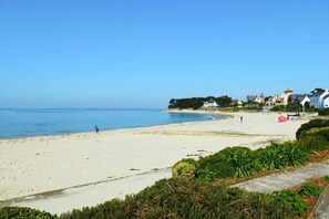 Une plage avec un ciel dégagé, un rivage sablonneux et des maisons en arrière-plan.