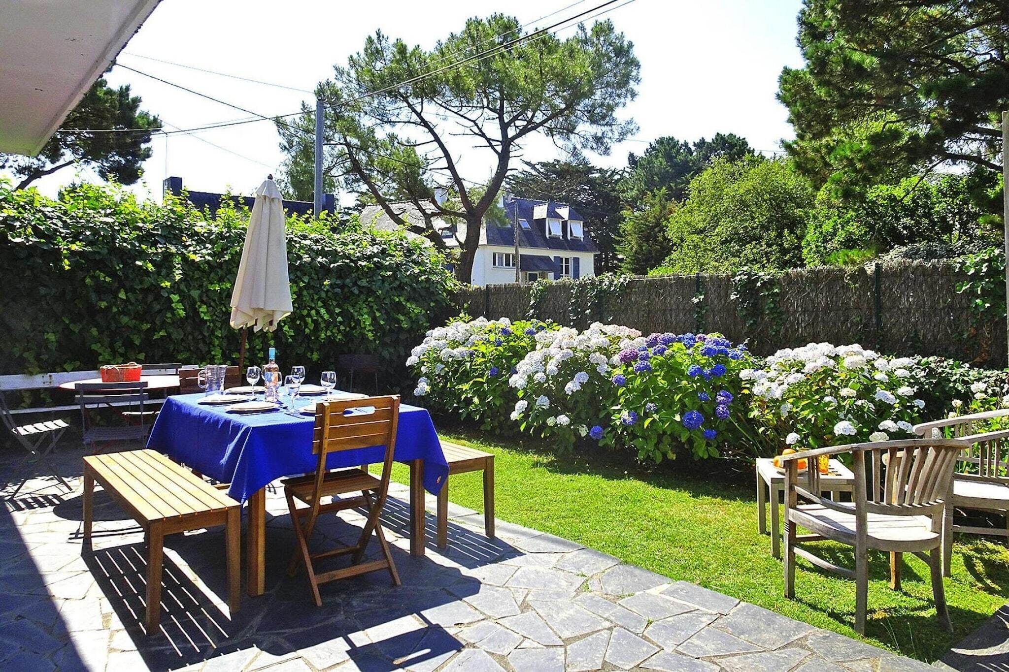 An outdoor patio with a table set for dining, surrounded by lush greenery and flowering plants.