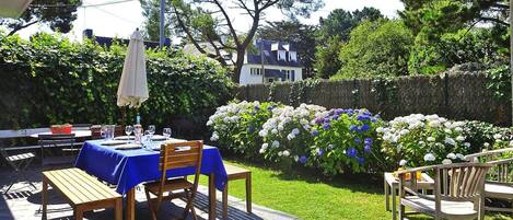 An outdoor patio with a table set for dining, surrounded by lush greenery and flowering plants.