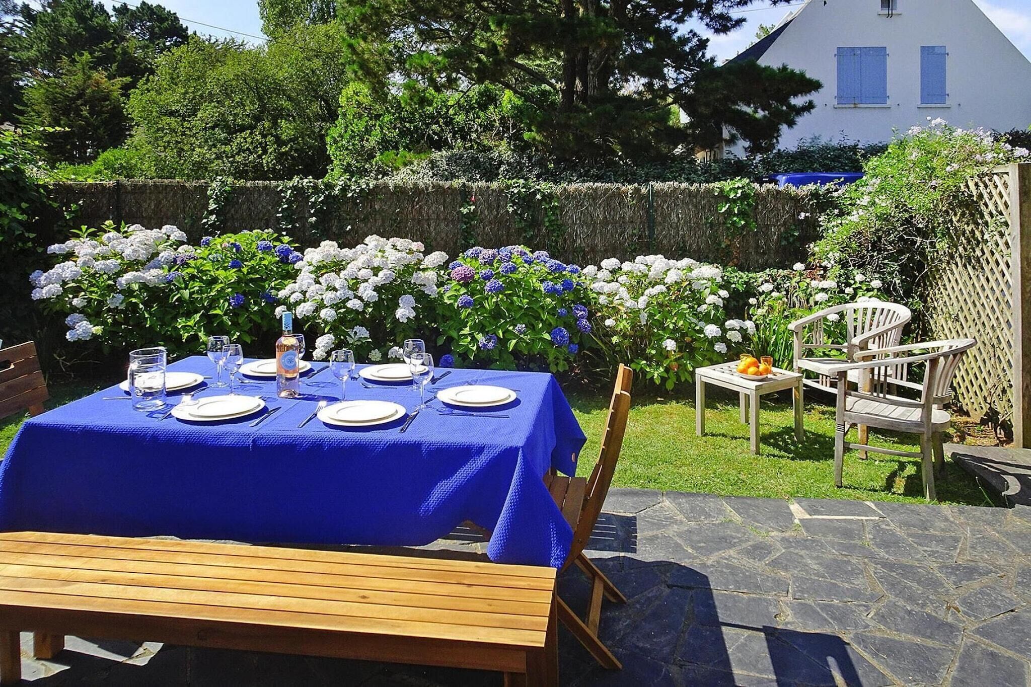 Un área de comedor al aire libre con una mesa dispuesta para cuatro personas, rodeada de abundante follaje y plantas en flor.