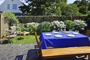 Un espace de restauration en plein air avec une nappe bleue, une table dressée pour quatre personnes, entourée de fleurs blanches et bleues.
