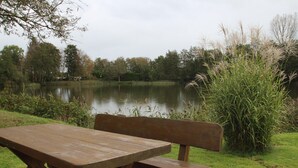 Une table et un banc en bois, installés près d’un lac paisible, entourés de verdure.