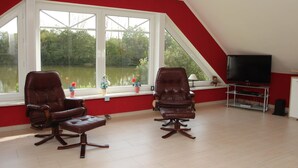 Une pièce avec deux fauteuils en cuir, un téléviseur et une fenêtre donnant sur un lac.