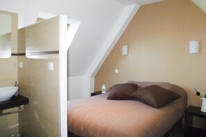 Une chambre à coucher comprenant un lit, une table de chevet, une commode, une lampe, et une salle de bain avec un lavabo et un miroir.