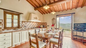 A spacious kitchen with a large island, wooden cabinets, and a view of the countryside through an open door.