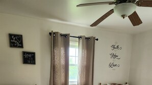Une chambre avec deux lits, un ventilateur de plafond et une petite table avec une lampe.
