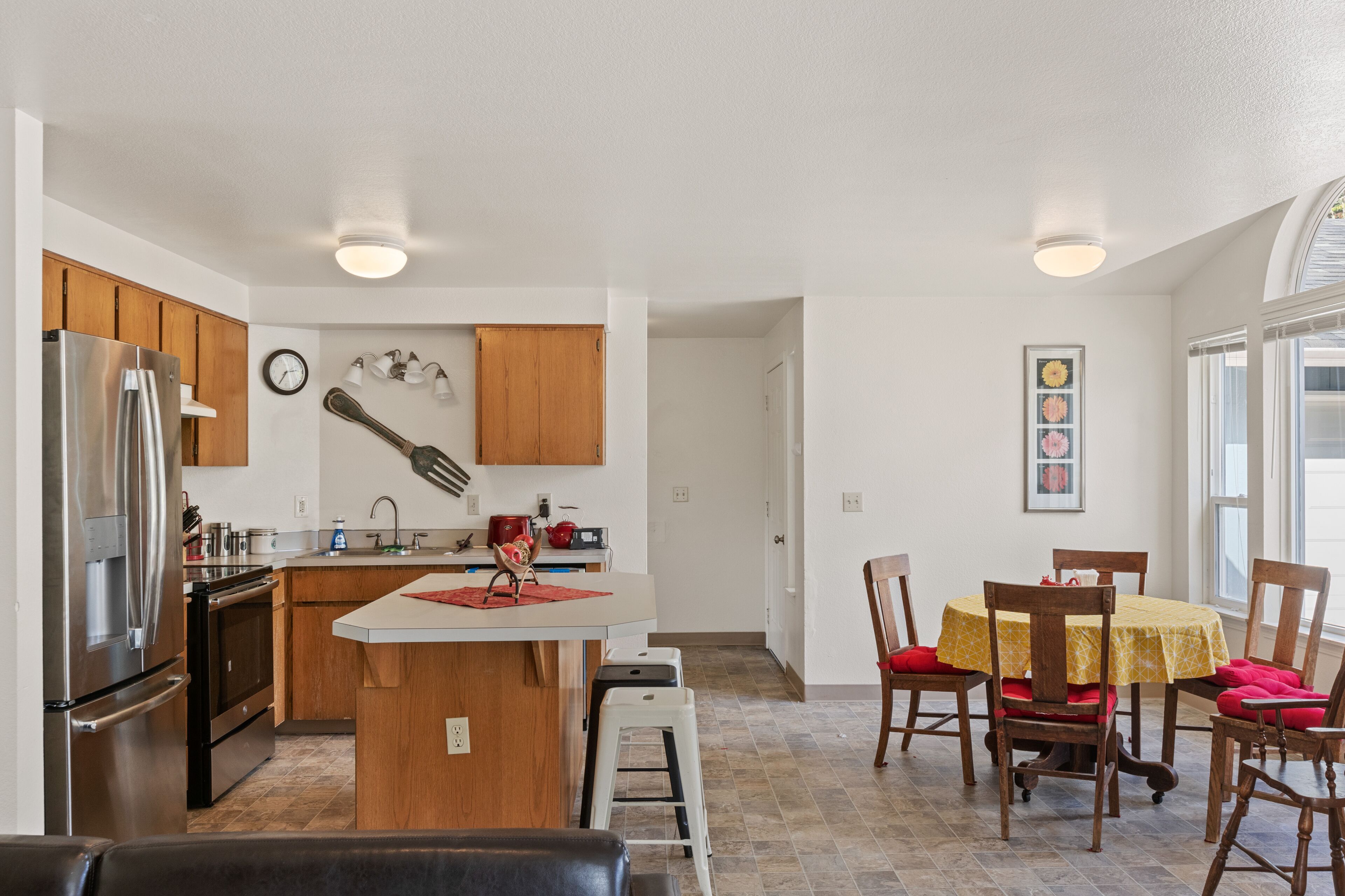 A modern kitchen with a central island, wooden cabinets, stainless steel appliances, and a dining area with a table and chairs.