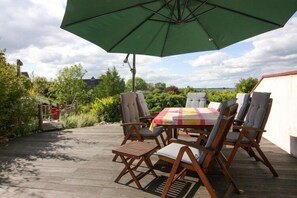 An outdoor patio with a table and chairs, a green umbrella, and a view of the surrounding greenery and buildings.