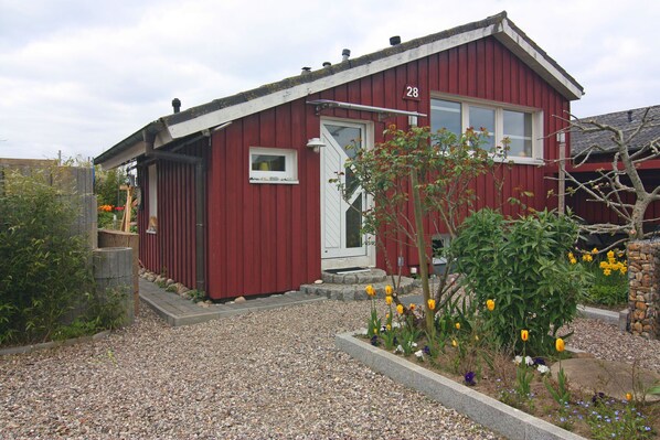 A red building with a white door and window, number 28, surrounded by gravel and a garden with flowers.