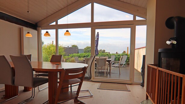 Un comedor con una mesa y sillas, techo de madera y vistas amplias a una terraza exterior.